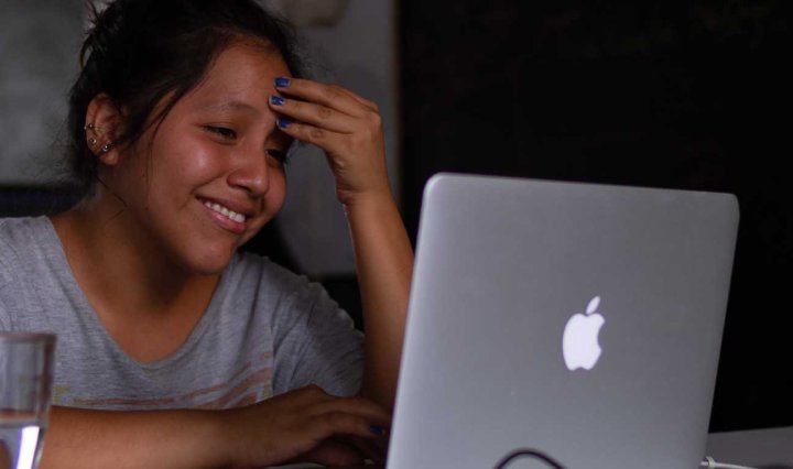 A Brown Latina smiles and holds her fingers to her head as she looks at her laptop