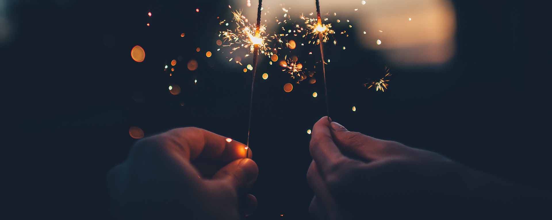 Two white hands hold us sparklers in the darkness