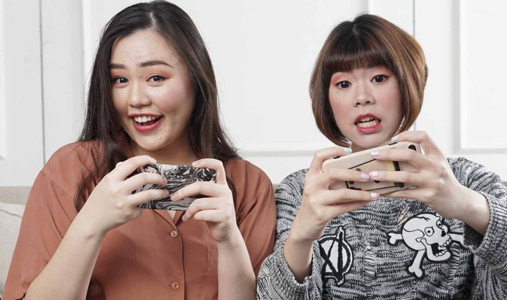 Two Asian women are playing a game on their mobile phones and they looked amused